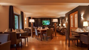 Un restaurante con varias mesas y sillas, una pantalla de televisión y lámparas fijadas a la pared.