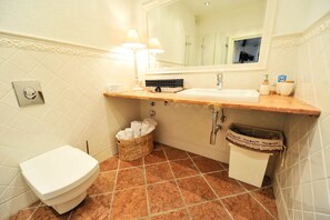 Bathroom features a toilet, sink, and mirror, with a tile design and storage.