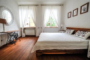 Classic bedroom with a wooden bed, round mirror, and small table with a lamp.