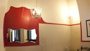 A bathroom with a red accent wall, a chandelier, a freestanding bathtub, and a sink with a towel rack. - Casalicchio B&B (Trapani)