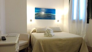 A hotel room with a bed, two pillows, a bedside table with a remote control, and a painting of waves on the wall. - Casalicchio B&B (Trapani)