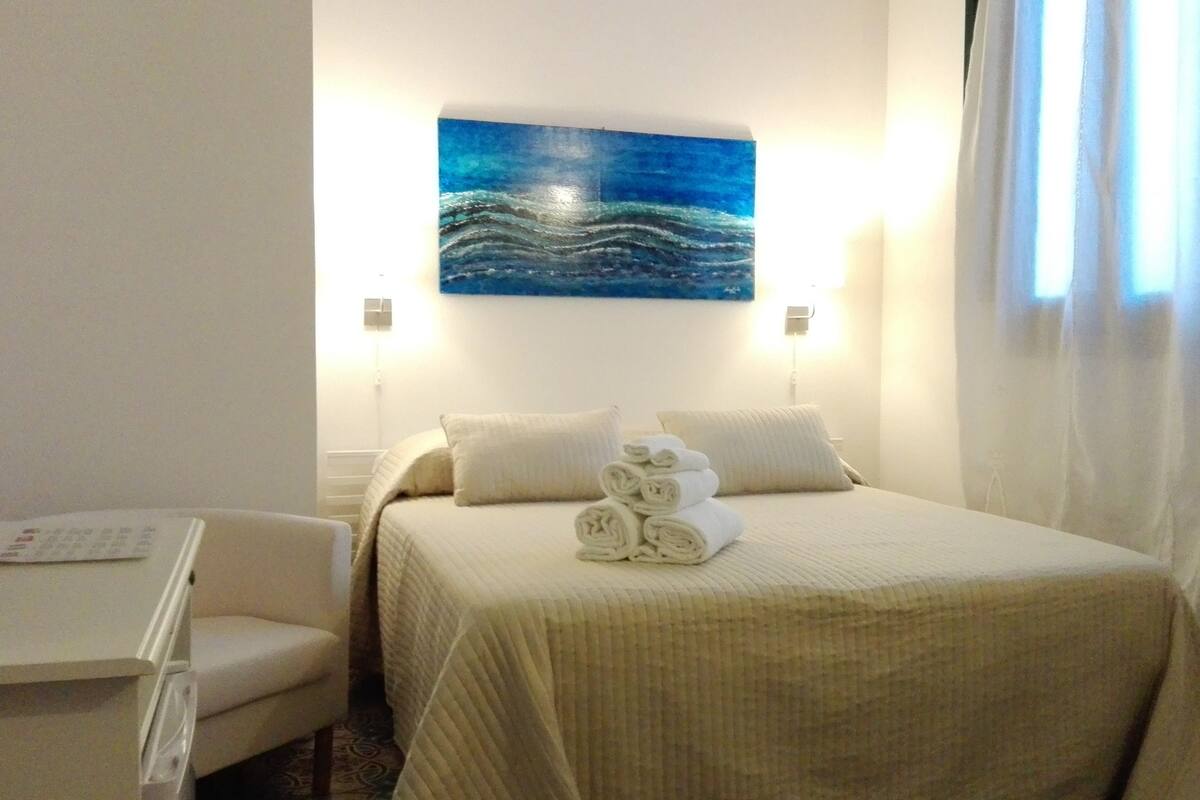 Ein Hotelzimmer mit einem Bett, zwei Kissen, einem Nachttisch mit Fernbedienung und einem Wellenbild an der Wand.