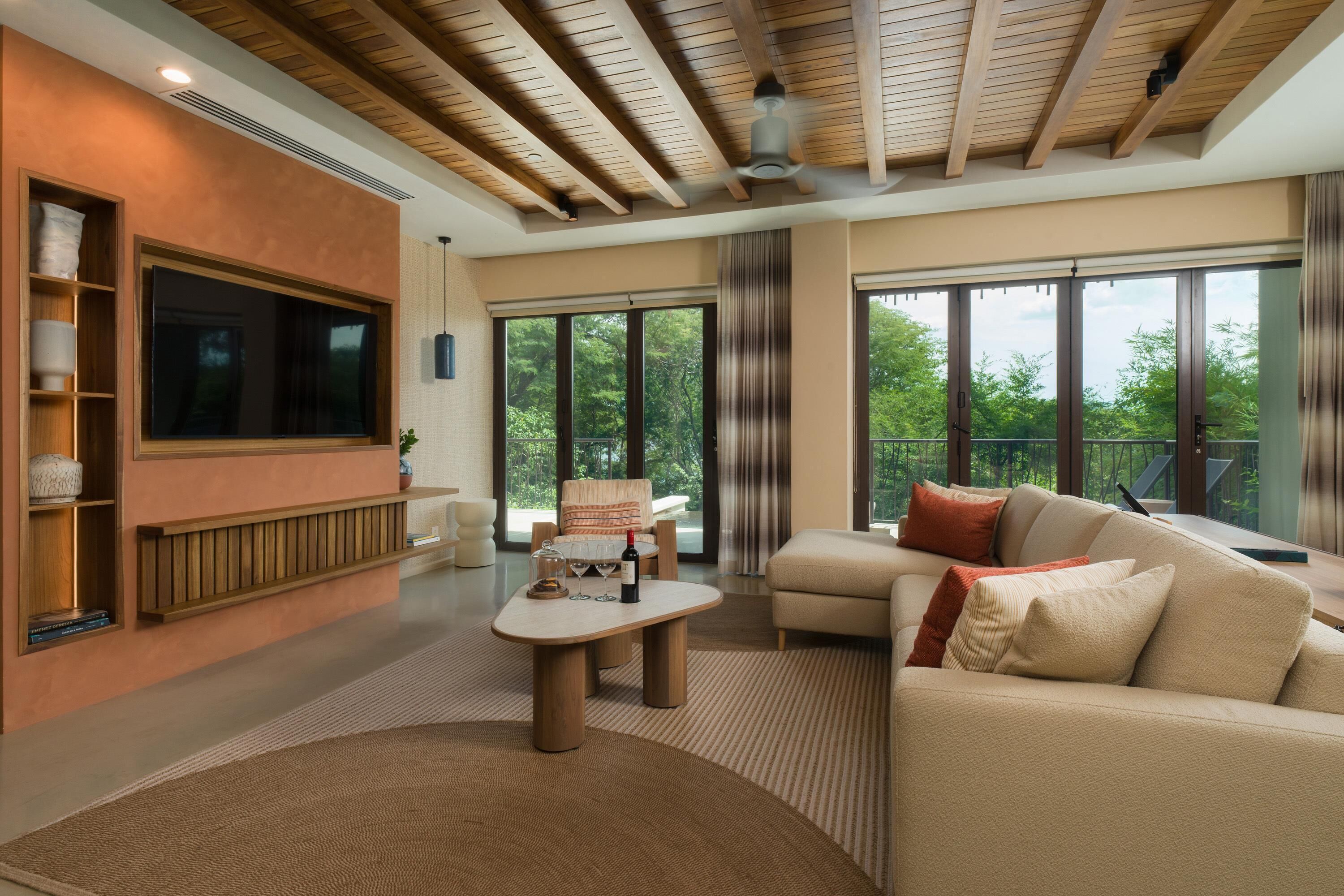 A modern living room with a large TV, comfortable seating, and large windows.