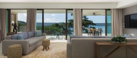 Un soggiorno moderno con divano, poggiapiedi e tavolino da caffè, ampie finestre con vista mare e una ventola a soffitto.