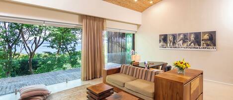 A modern living room with a large window, a sofa, a wooden coffee table, and a wooden cabinet.