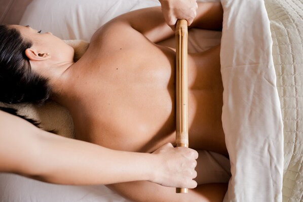 A person lying on a bed with a wooden massage tool.
