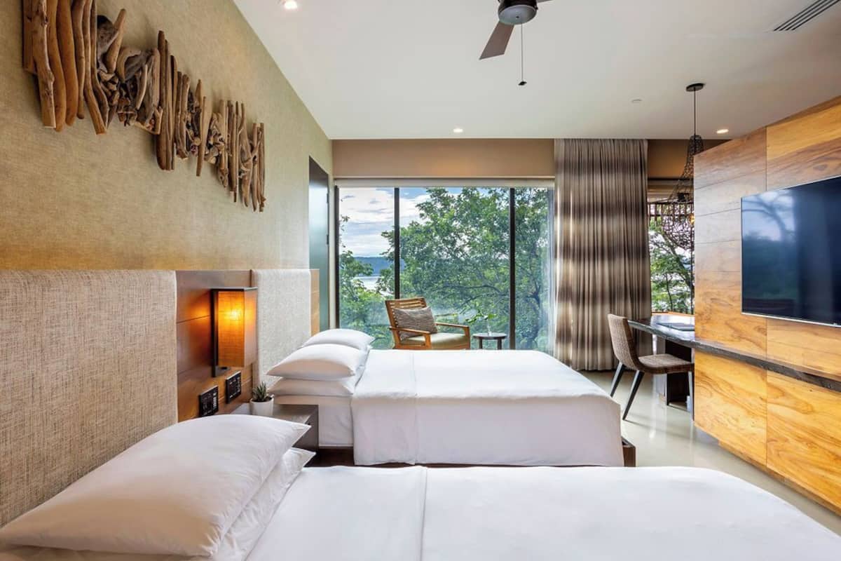 Ein modernes Hotelzimmer mit zwei Betten, einem großen Fernseher und Blick ins Freie.