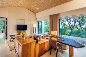 A modern kitchen with a wooden island, a flat-screen TV, and a large window offering a view of greenery.