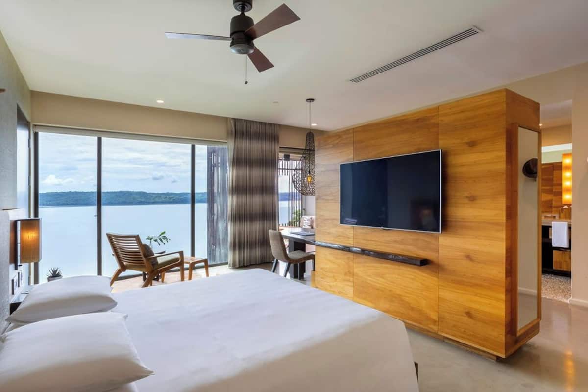 Ein modernes Hotelzimmer mit einem großen Bett, einem Schreibtisch, einem Fernseher und Blick auf das Wasser.
