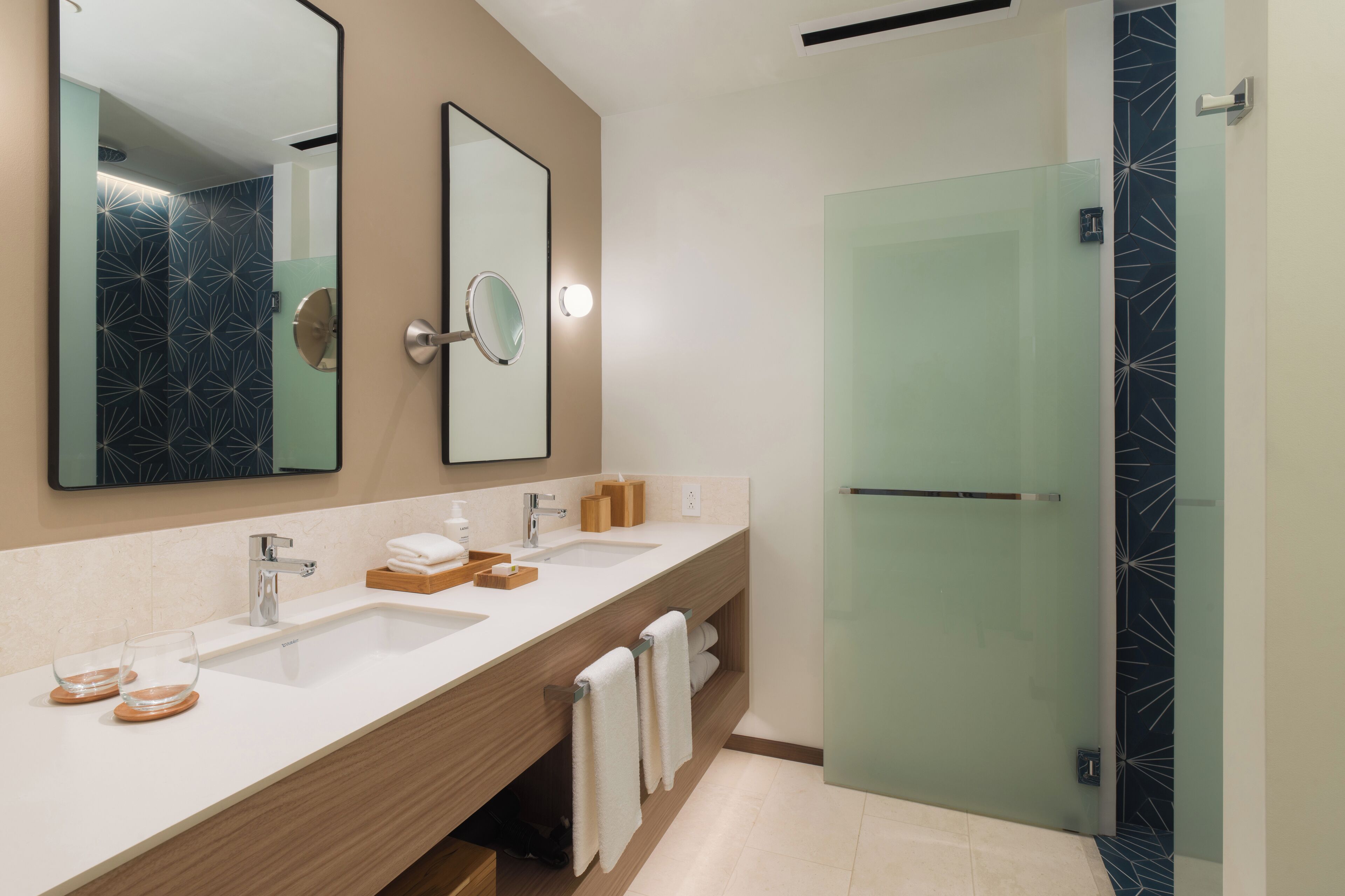 A modern bathroom with two sinks, a large mirror, and a glass shower enclosure.
