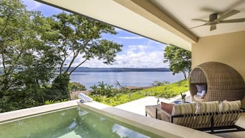 A pool with a view of the sea, a wicker chair, and a ceiling fan.