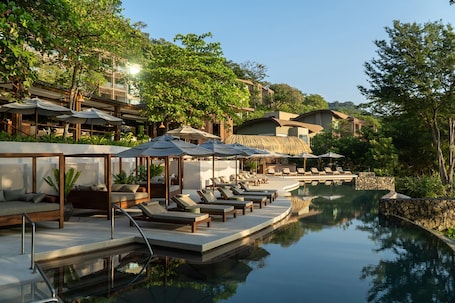 A resort with a pool, lounge chairs, umbrellas, and a stone wall.