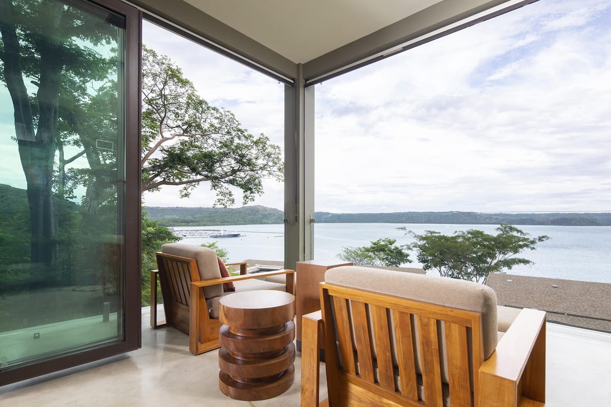 Ein modernes Zimmer mit großen Fenstern, Holzmöbeln und Blick auf einen See und Hügel.