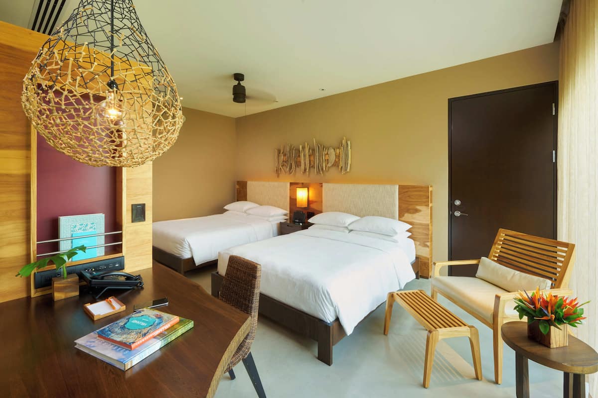Ein Hotelzimmer mit zwei Betten, einem Holztisch, einem Stuhl, einem kleinen Tisch und einer dekorativen Pendelleuchte.