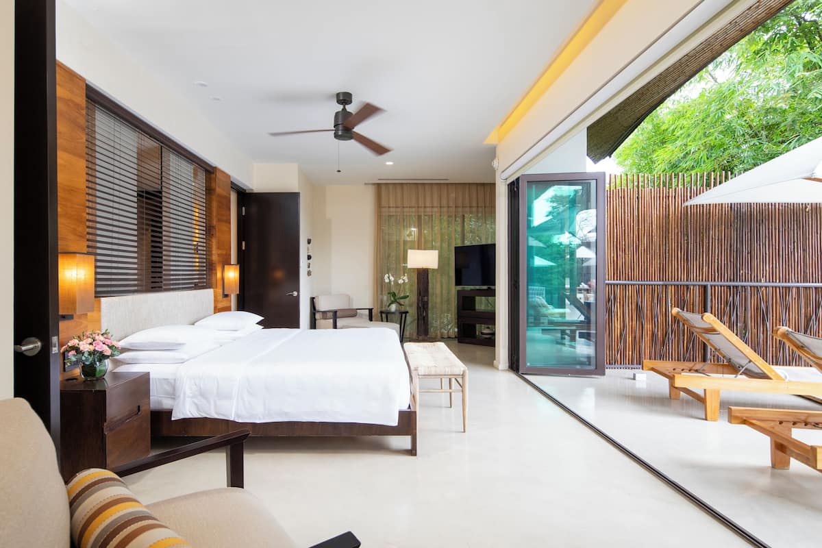Ein modernes Hotelzimmer mit einem großen Bett, einem Deckenventilator, einem Fernseher und einem Balkon mit Liegestühlen.