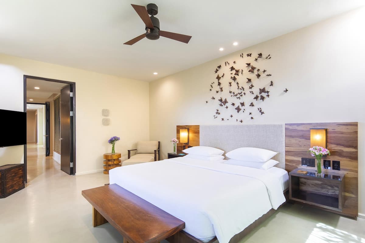 Ein modernes Hotelzimmer mit einem großen Bett, Nachttischen, einer Bank, einem Deckenventilator und einer Wandleuchte.