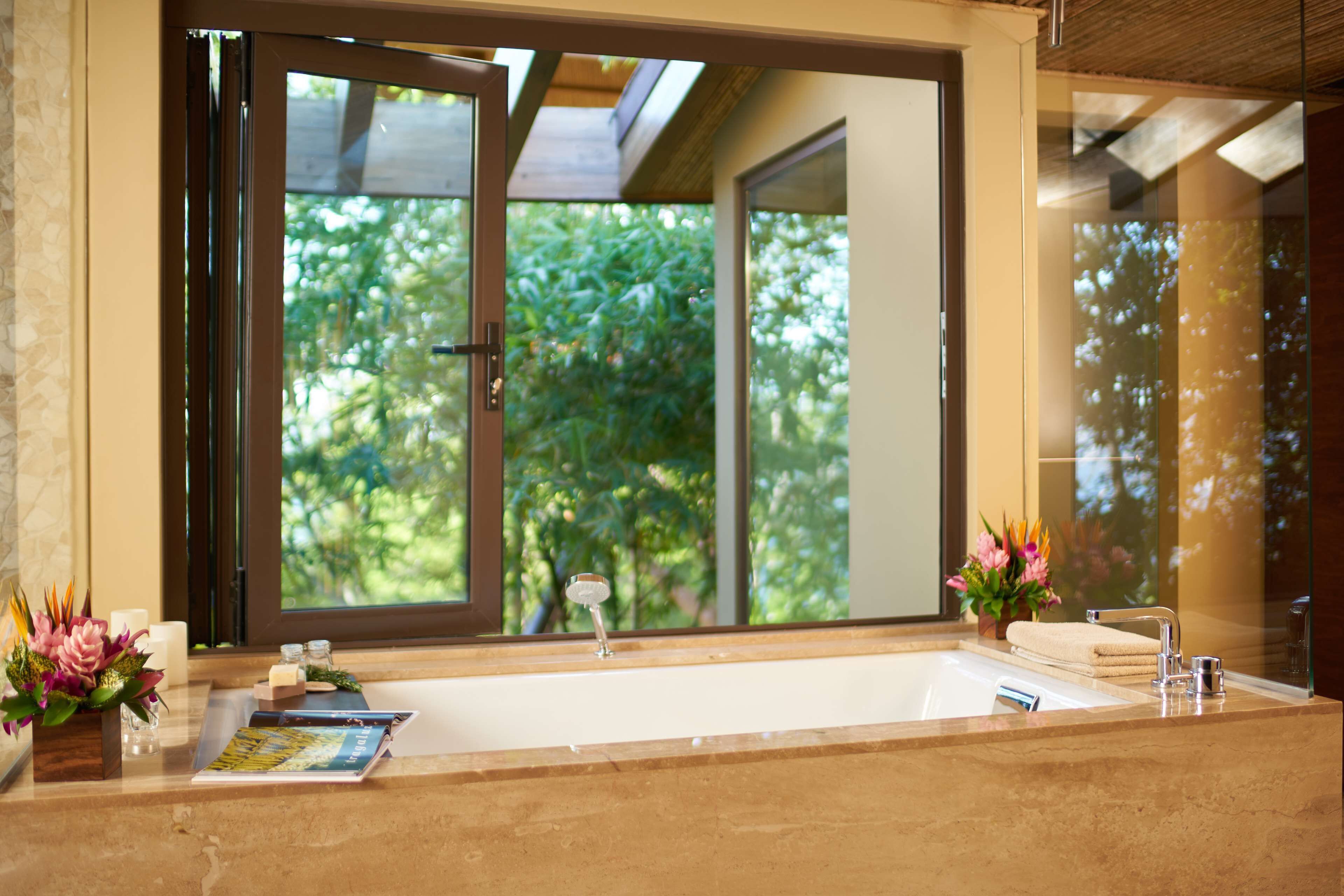 A bathroom with a large window, a bathtub, a sink, and a mirror.