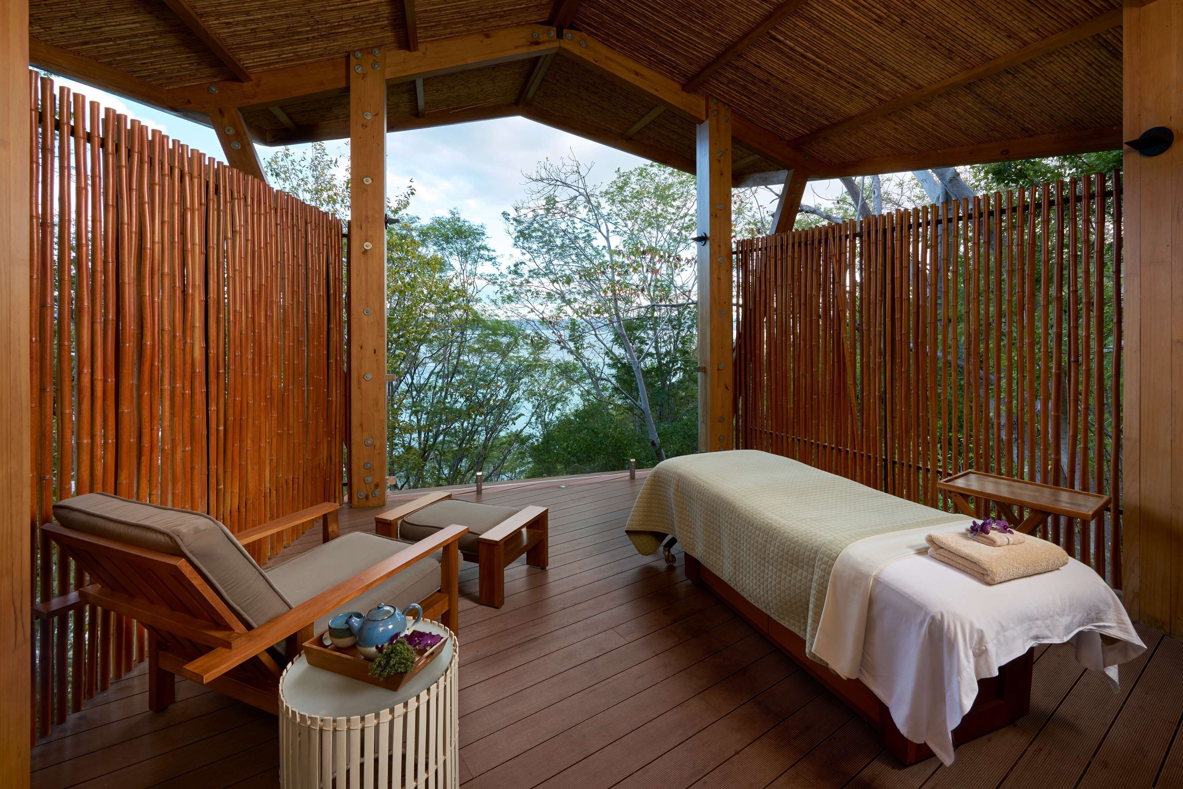 A wooden deck with a bed, lounge chairs, and a small table with a tray of items.