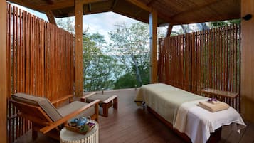 A wooden deck with a bed, lounge chairs, and a small table with a tray of items.