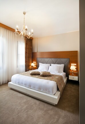 Ett modernt hotellrum med en stor säng, en kristallkrona och två sängbord med lampor.