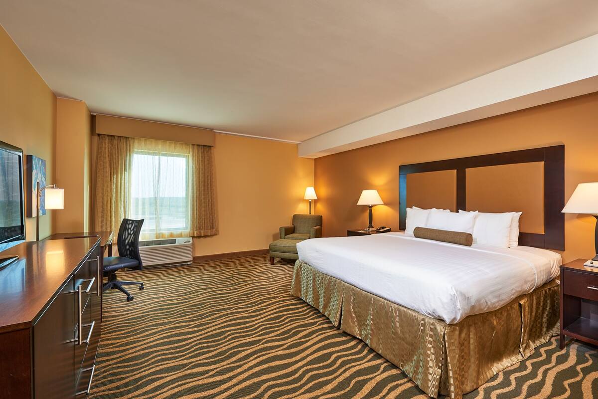 A hotel room with a large bed, a desk with a chair, two bedside lamps, and a television.
