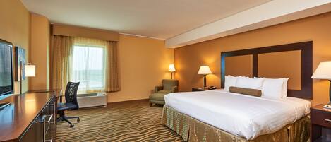 A hotel room with a large bed, a desk with a chair, two bedside lamps, and a television.