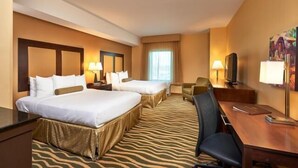 Quarto de hotel com duas camas, uma mesa, uma cadeira e uma televisão.