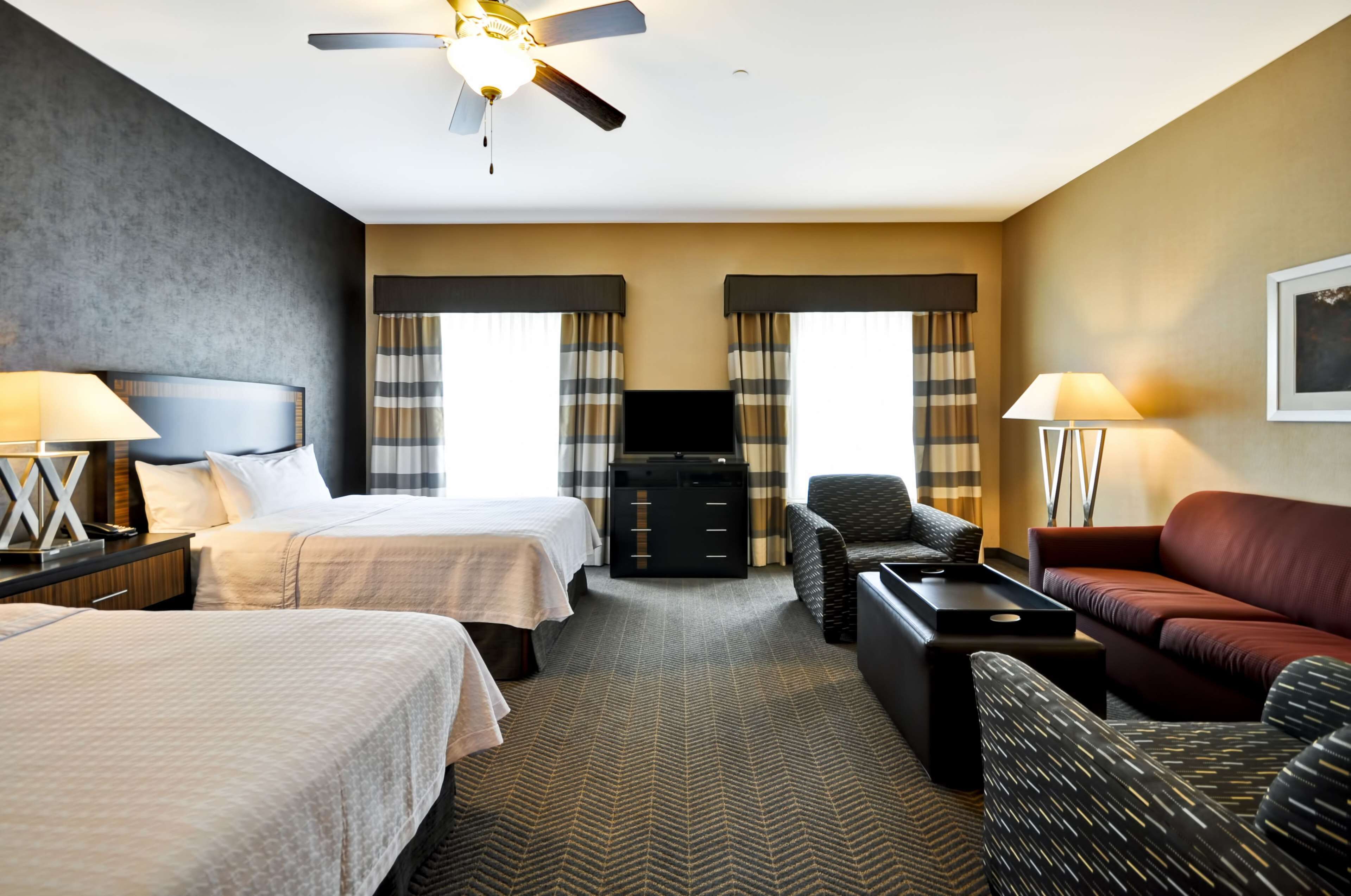 A hotel room with two beds, a sofa, a TV, and a ceiling fan.