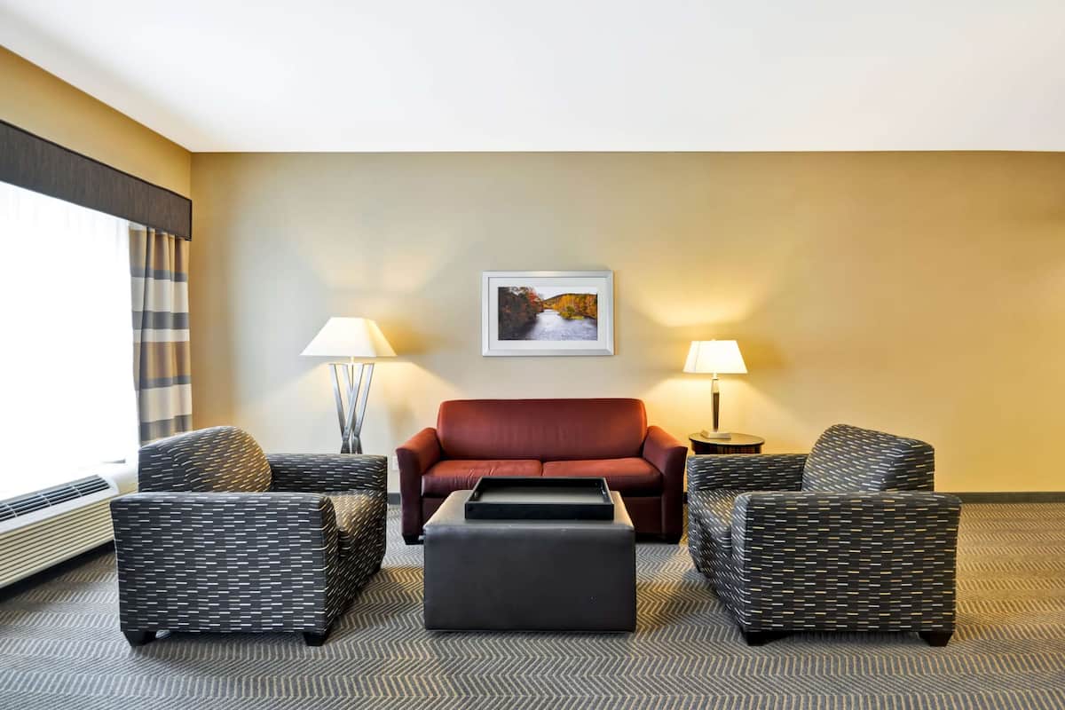 Une chambre d’hôtel avec un canapé rouge, deux fauteuils à motifs, un pouf noir et un tableau encadré au mur.