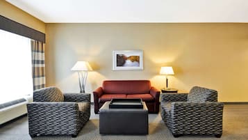 Habitación de hotel con un sofá rojo, dos sillones estampados, un reposapiés negro y un cuadro enmarcado en la pared.