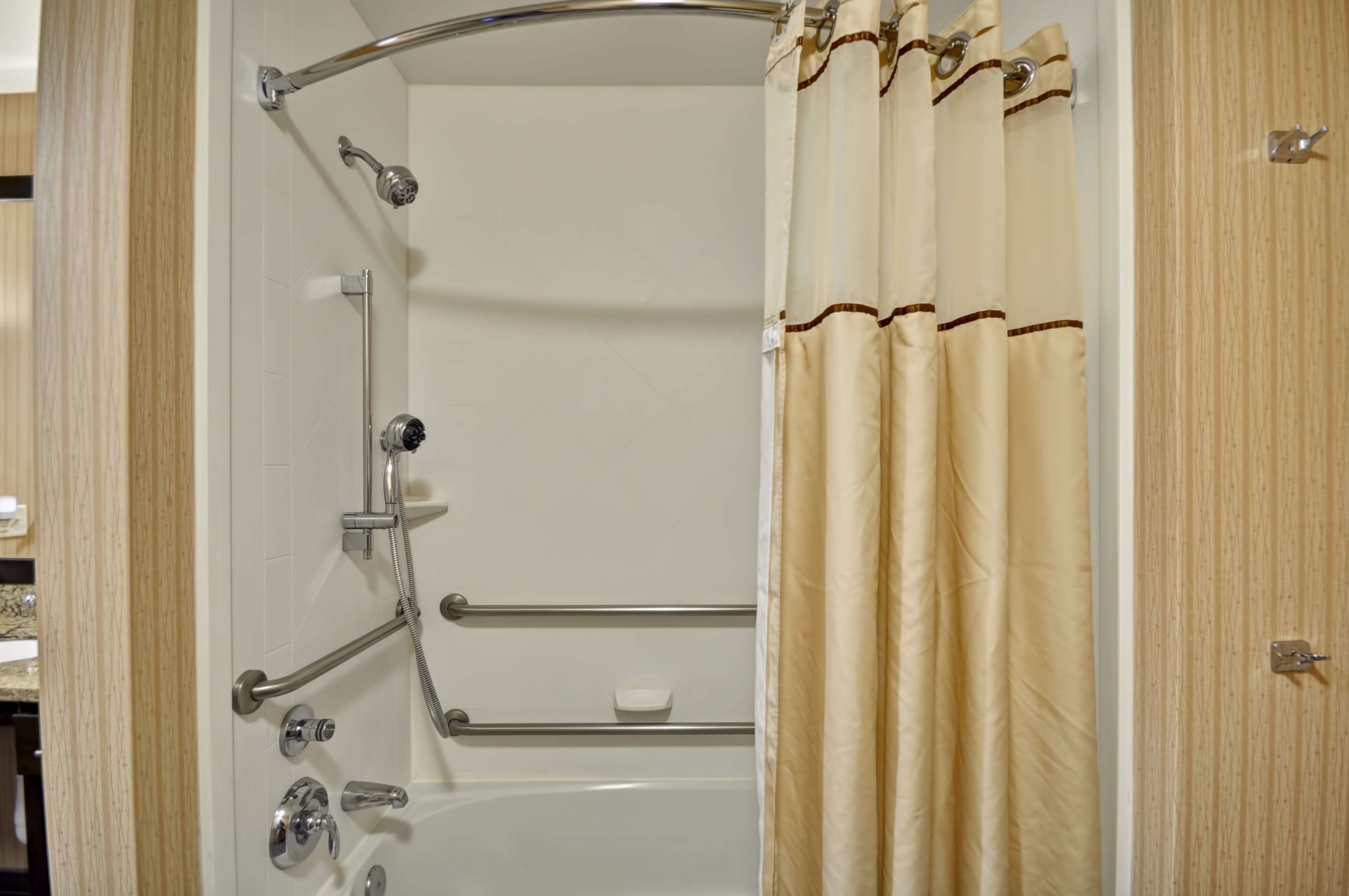 A shower area with a grab bar, a handheld showerhead, and a handheld faucet.