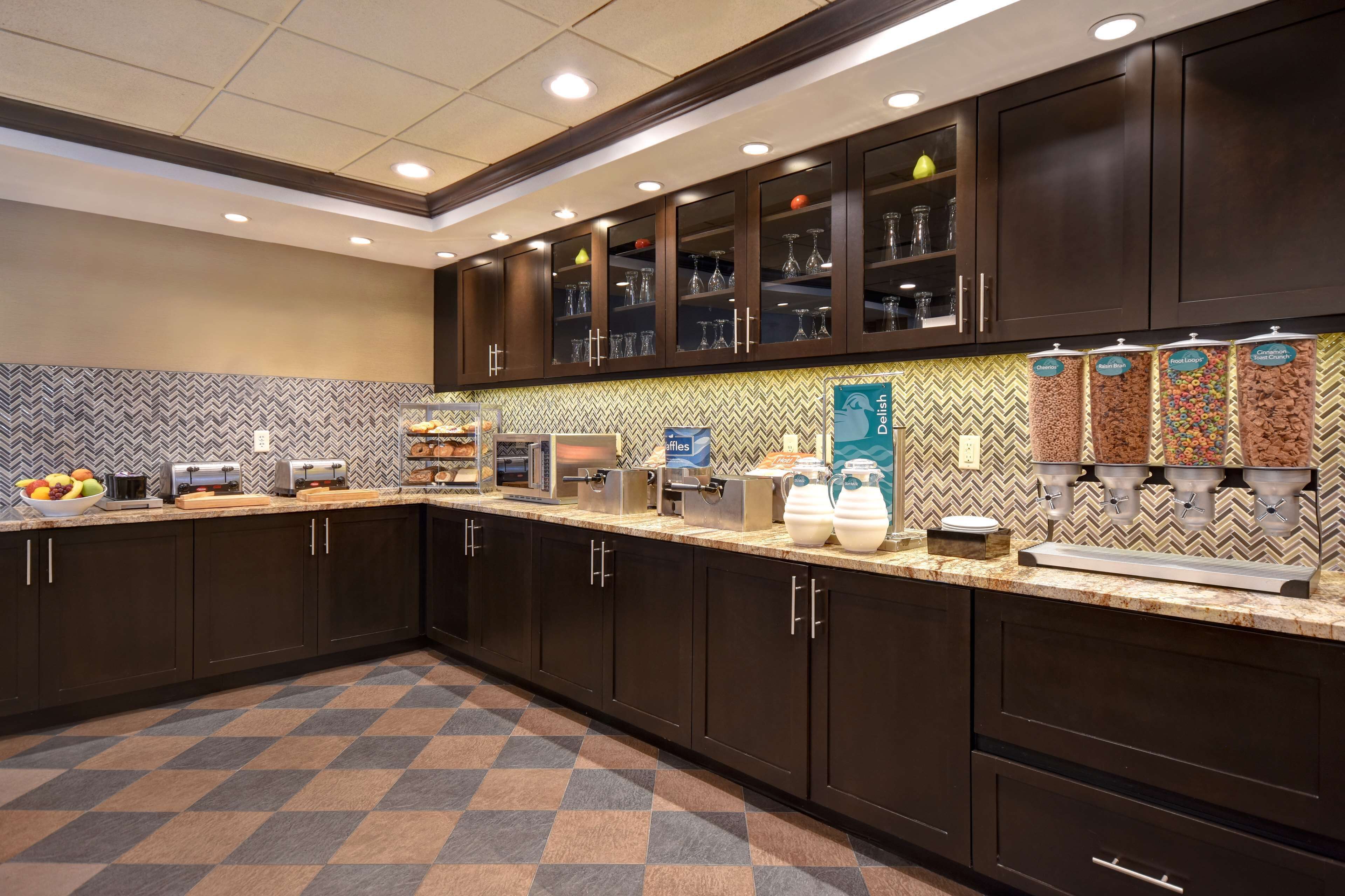 A hotel kitchen with dark cabinets, a herringbone tile backsplash, and a checkered floor pattern.