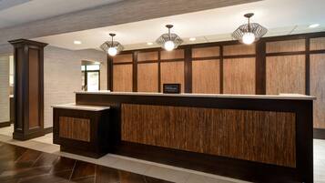 A modern hotel reception desk with a wood panel design, a sign indicating it's a Hilton Honors hotel, and a clean, tiled floor.