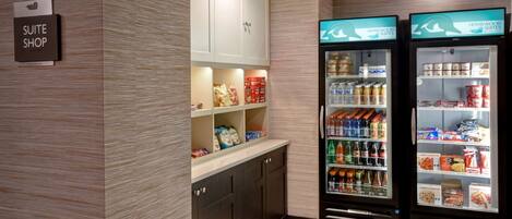 A hotel suite shop with a sign, a kitchenette, and two beverage dispensers.
