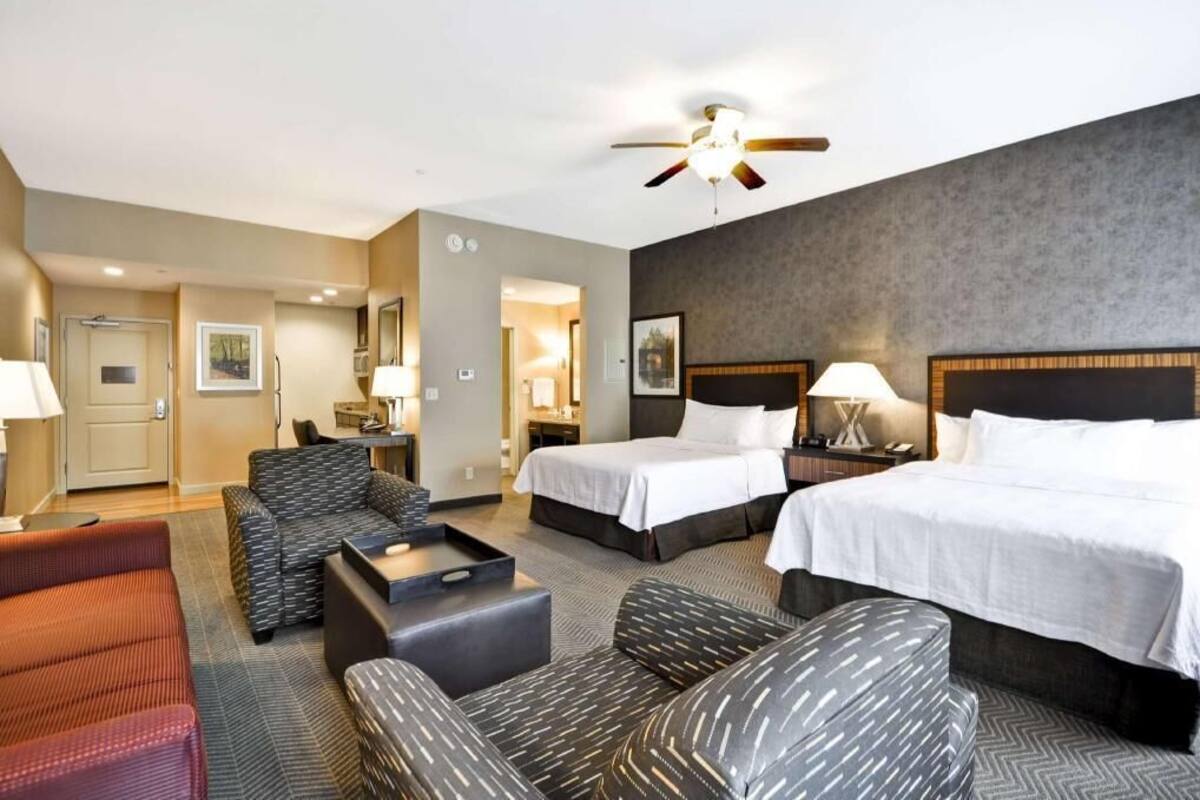 Une chambre d’hôtel avec deux lits, un canapé, une chaise, un bureau et un ventilateur de plafond.