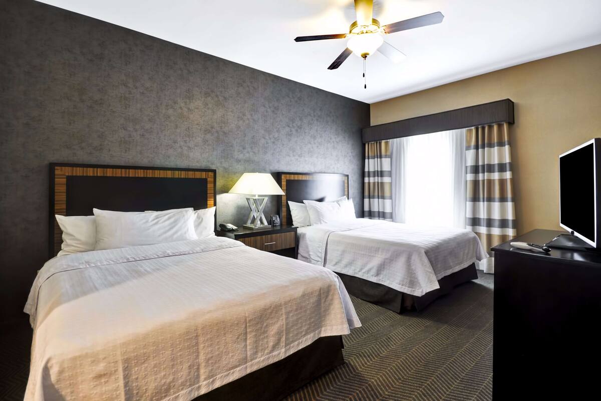 Une chambre d’hôtel avec deux lits, un bureau, une télévision et un ventilateur de plafond.