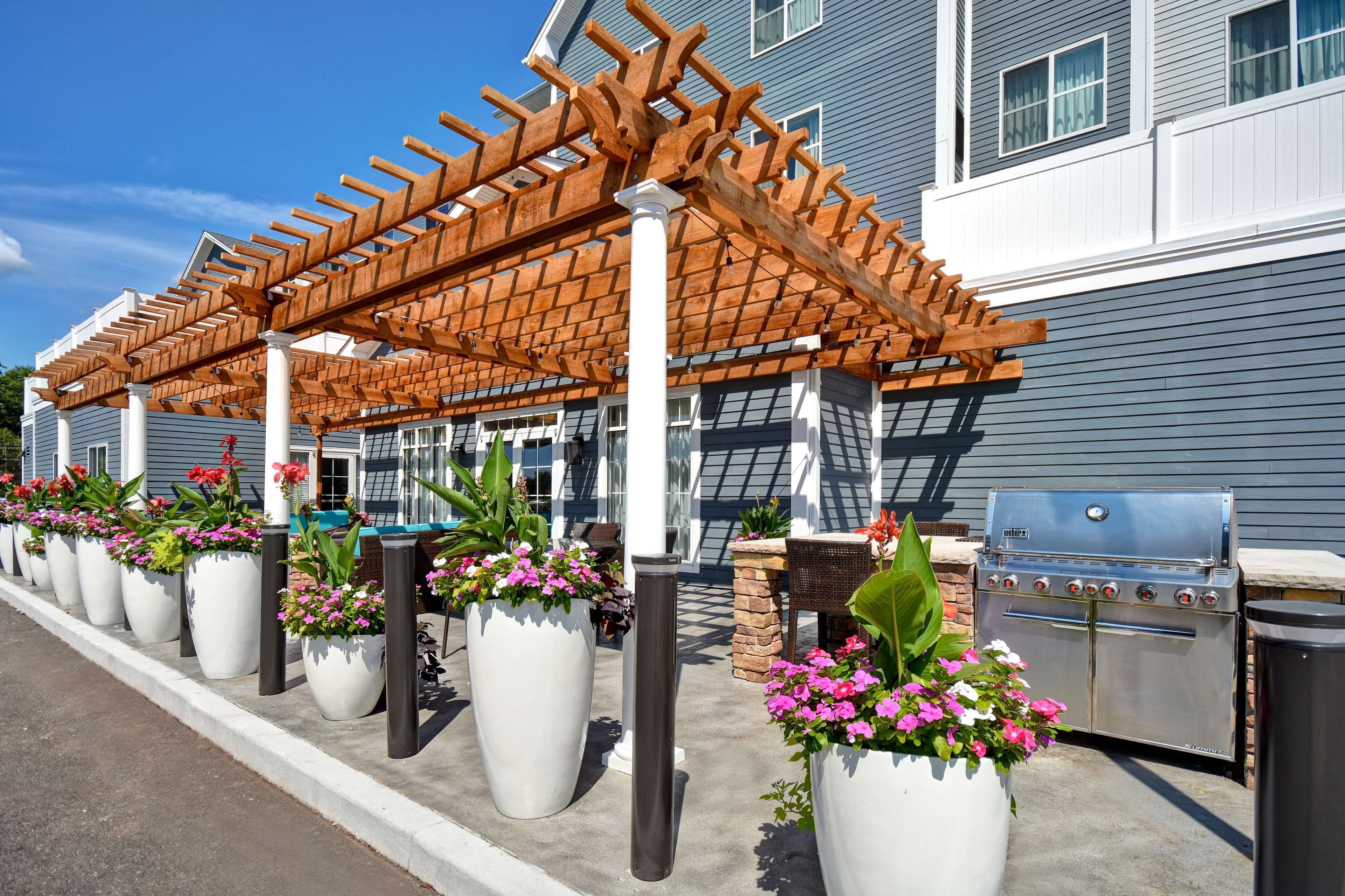 An outdoor patio area with a wooden pergola, potted plants, and a barbecue grill.