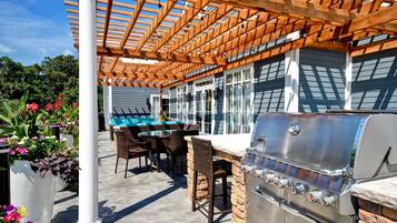 Une terrasse extérieure équipée d’un barbecue, de chaises en osier, d’une table de billard et d’une pergola.
