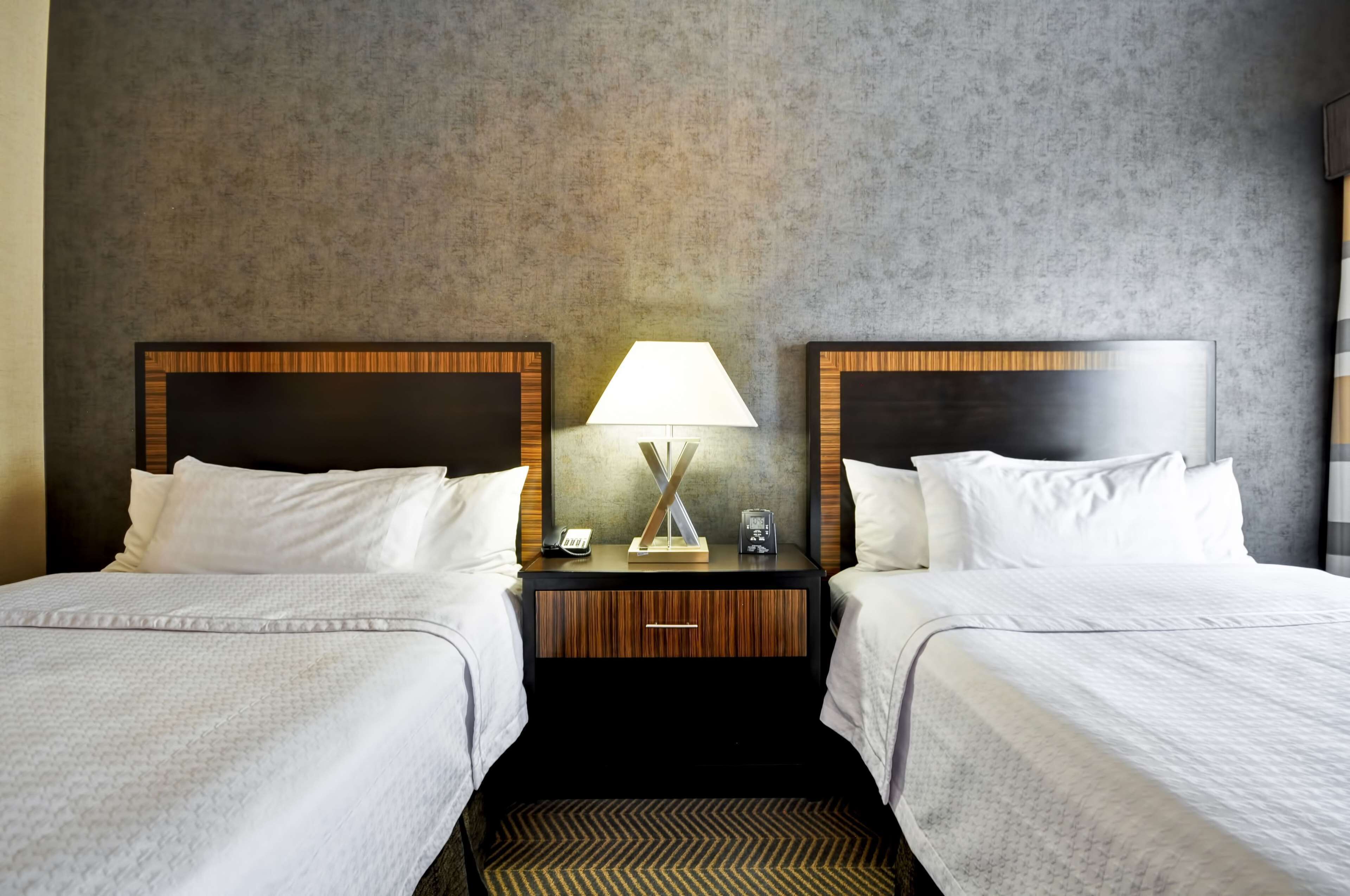Ein Hotelzimmer mit zwei Betten, einem Nachttisch mit Lampe und einer Wand mit Struktur.