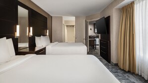 Una habitación de hotel con dos camas, un espejo grande, un televisor y un escritorio.