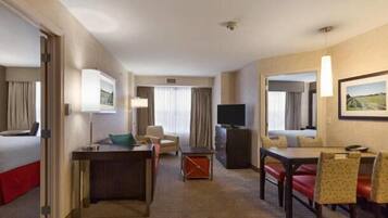 A hotel room with a bed, a desk, a chair, a TV, and a dining area with chairs and a table.