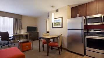 Habitación de hotel compacta con kitchenette, comedor con mesa y sillas, televisor y cama.