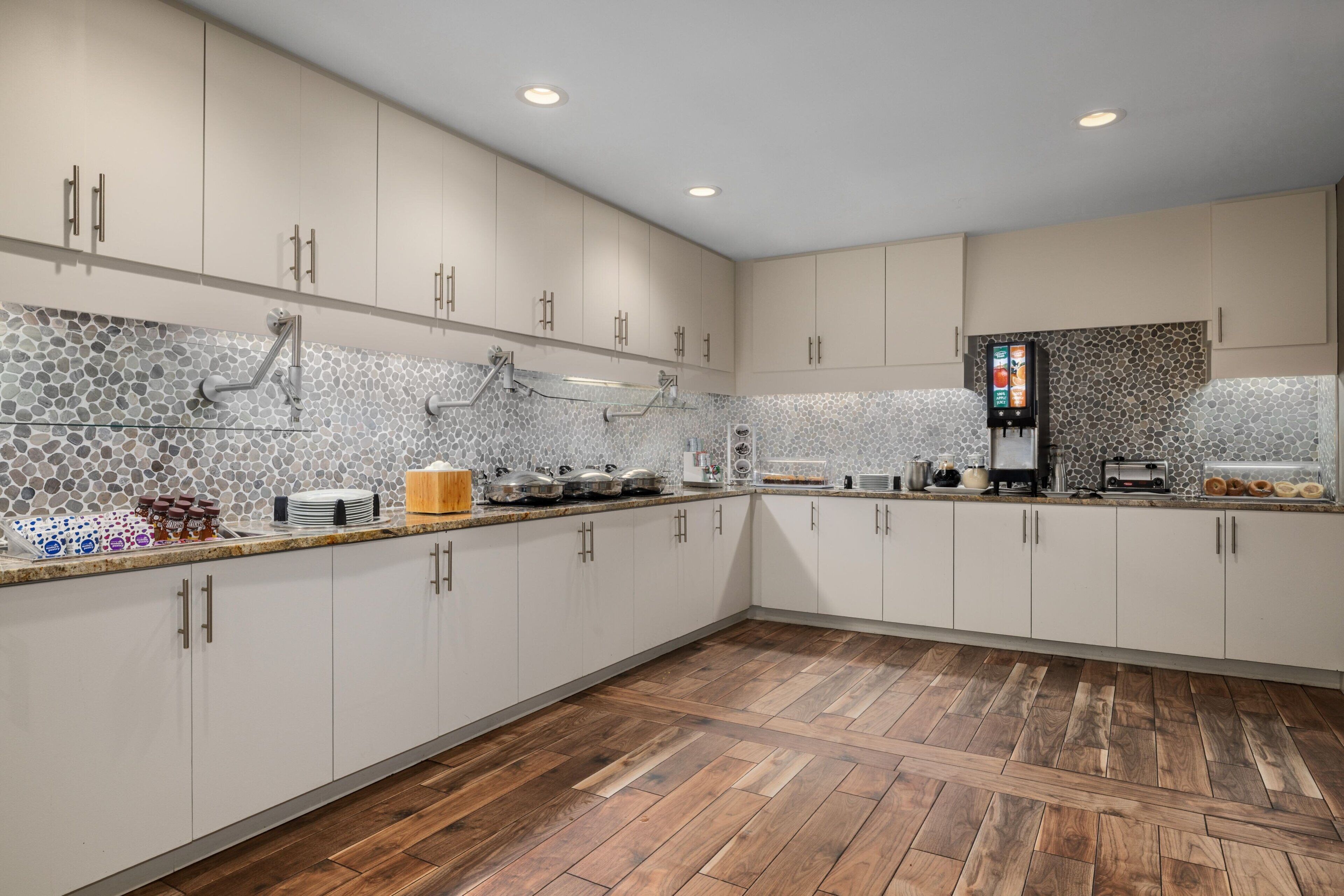 Una cocina moderna con armarios blancos, piso de madera en espiga y salpicadero de piedra.