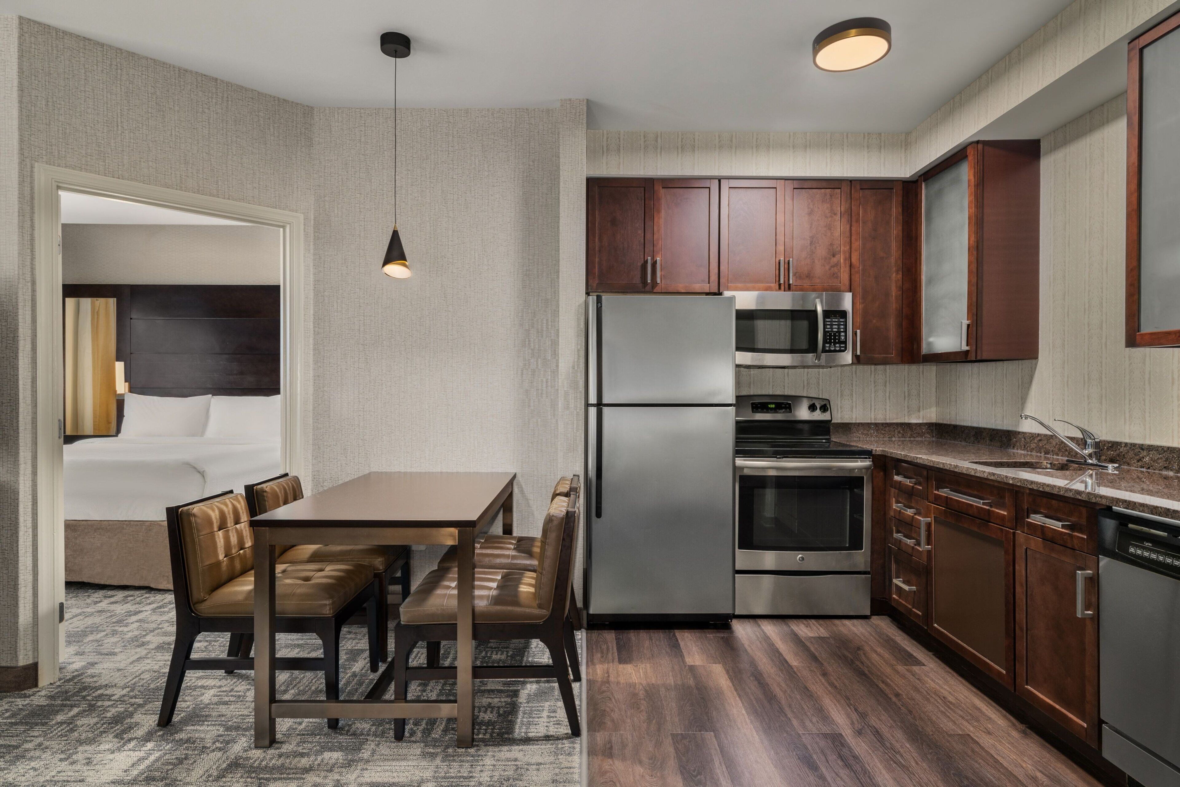 A compact kitchen with a refrigerator, microwave, oven, and dishwasher. There is a dining area with a table and chairs.