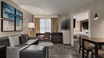 A modern hotel room with a sofa, a small round table, a desk, a TV, and a bed.