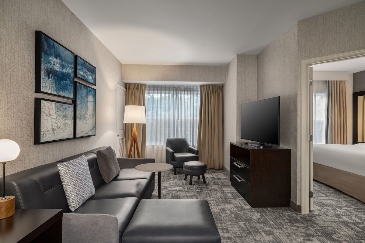 A modern hotel room with a sofa, a TV, a desk, and a lamp.