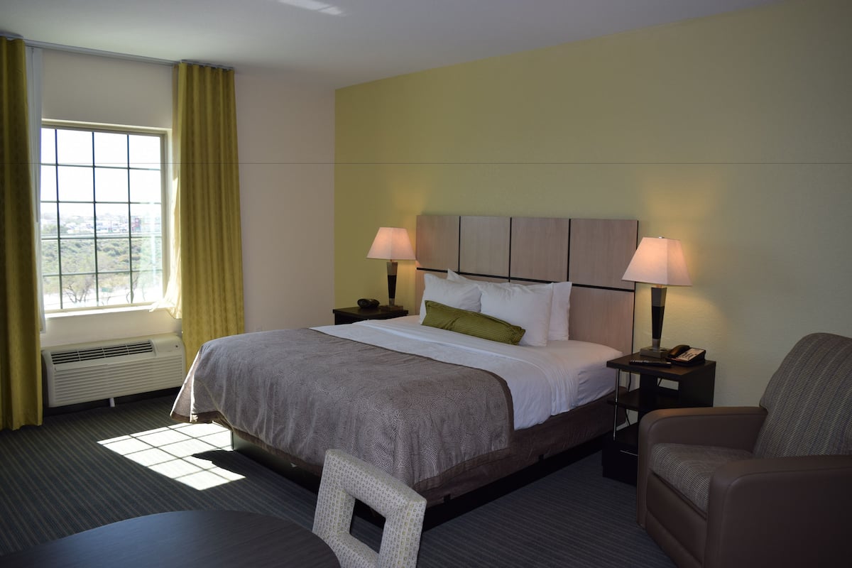 A hotel room with a bed, two bedside tables with lamps, a chair, and a window with curtains.