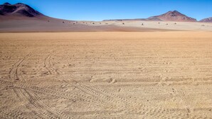 Un extenso paisaje desértico con dunas de arena y montañas bajo un cielo azul despejado.