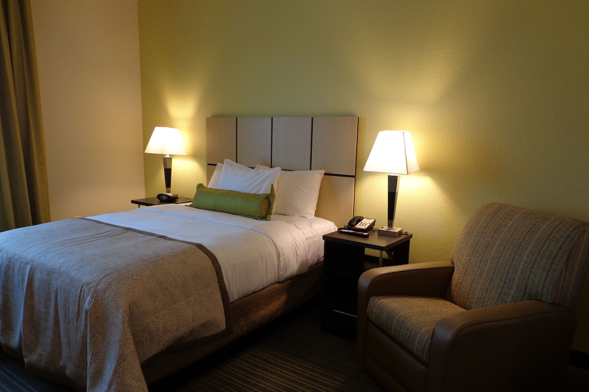 A hotel room with a bed, two bedside lamps, a telephone, and a chair.