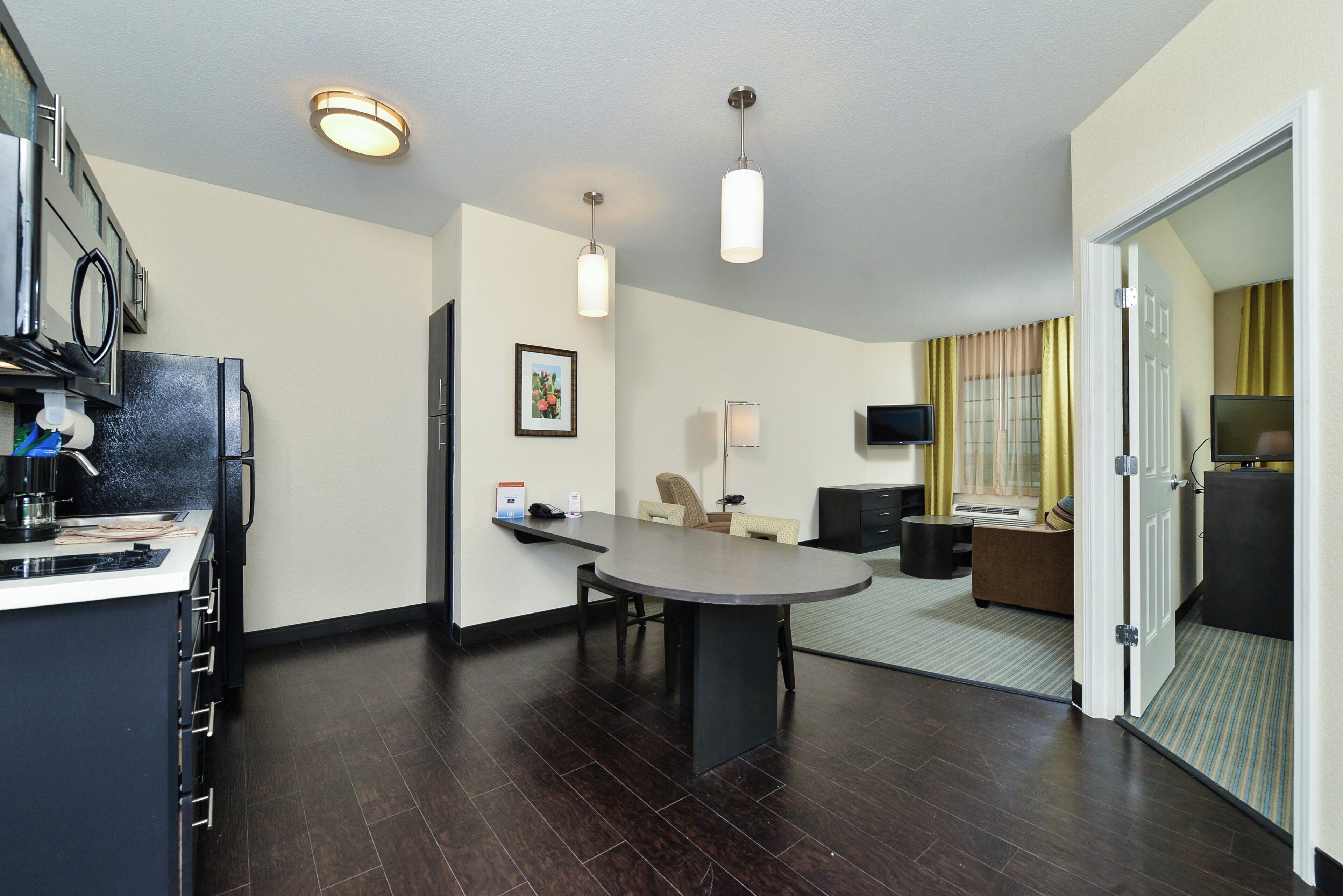 Una habitación de hotel moderna con zona de comedor, televisión de pantalla plana y un amplio ventanal con cortinas.